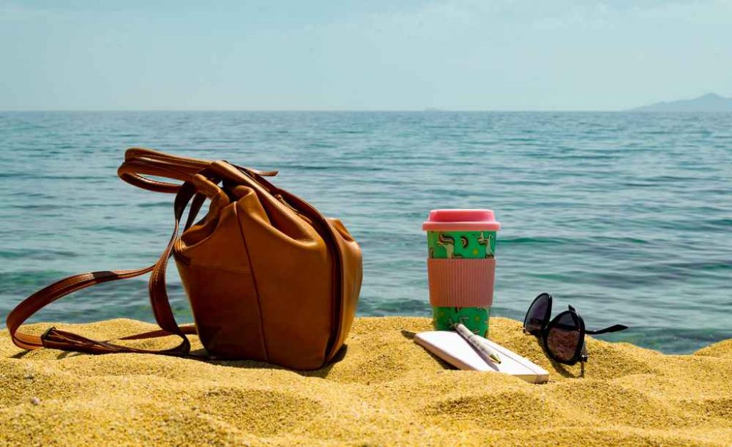Printed tumbler beside hand bag and glasses on a beach